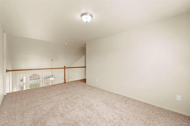 carpeted spare room featuring baseboards and vaulted ceiling