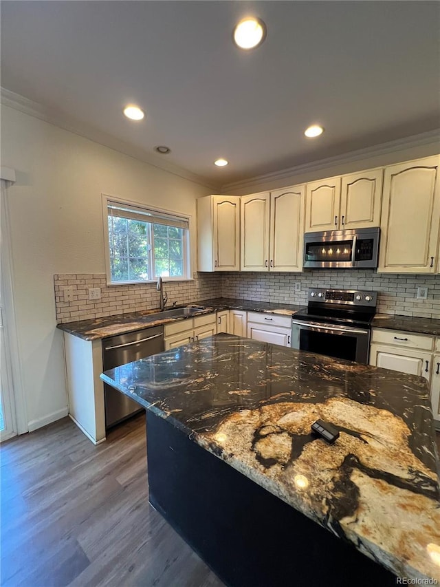 kitchen with appliances with stainless steel finishes, dark stone counters, ornamental molding, sink, and dark hardwood / wood-style floors