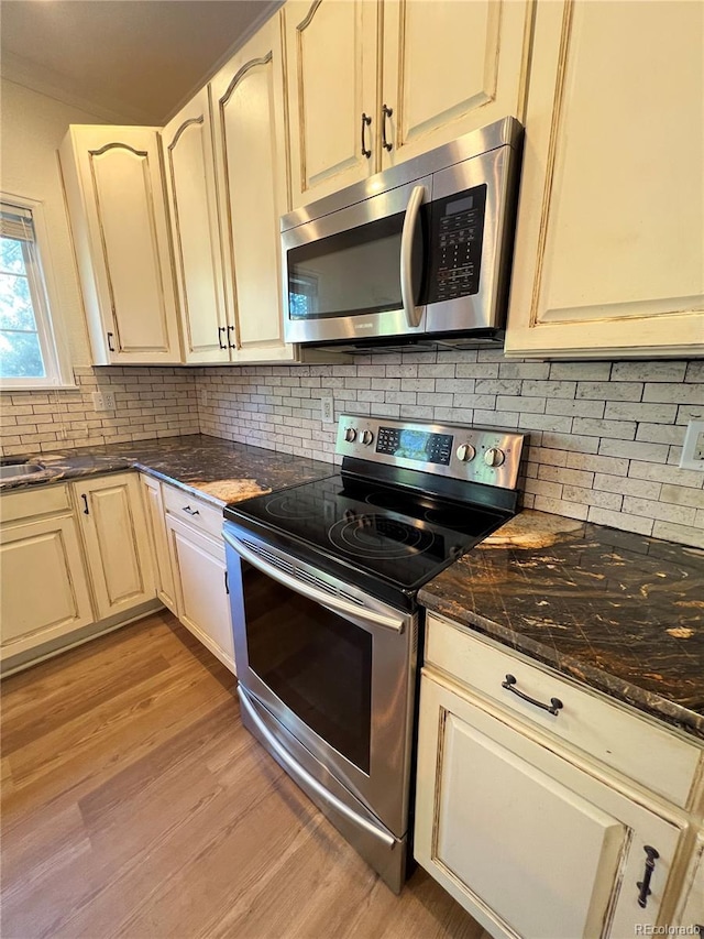 kitchen with tasteful backsplash, dark stone counters, stainless steel appliances, cream cabinets, and light hardwood / wood-style floors