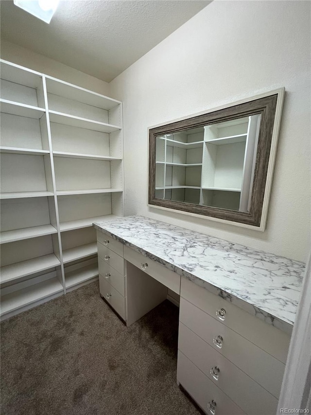 unfurnished office featuring a textured ceiling, built in desk, and dark carpet