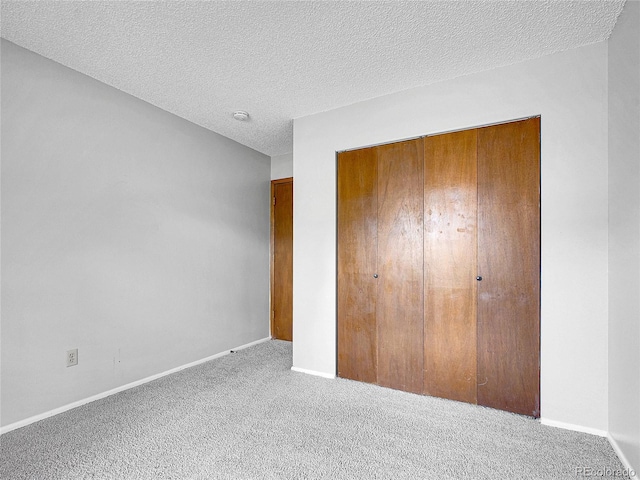 unfurnished bedroom with carpet floors, a textured ceiling, baseboards, and a closet