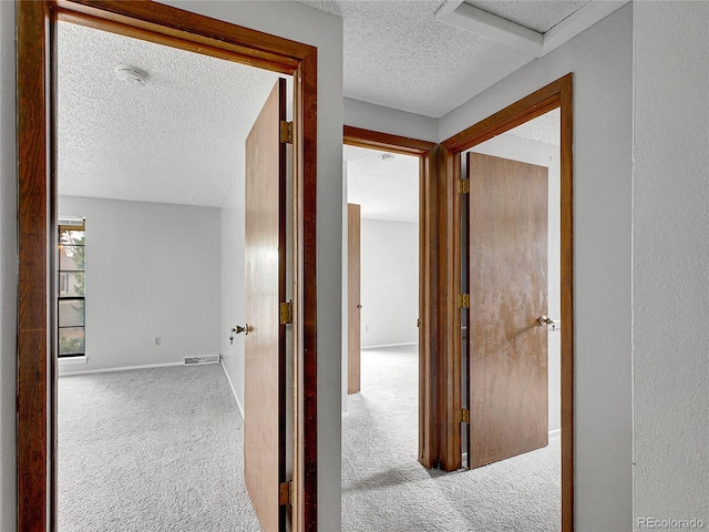 corridor with carpet flooring, a textured ceiling, visible vents, and attic access