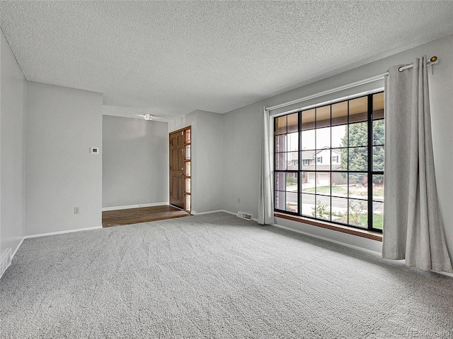spare room with carpet floors, a textured ceiling, visible vents, and baseboards