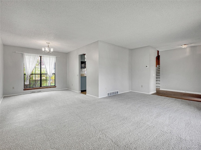 carpeted empty room with visible vents, a textured ceiling, baseboards, and a notable chandelier
