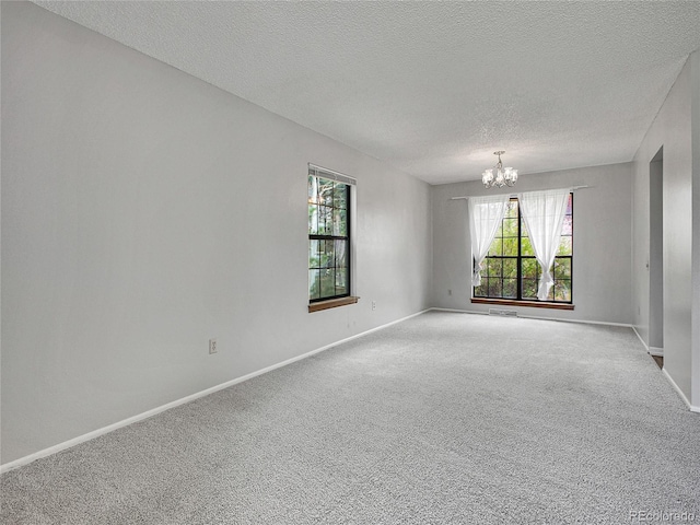 carpeted spare room featuring baseboards, a textured ceiling, a chandelier, and a wealth of natural light