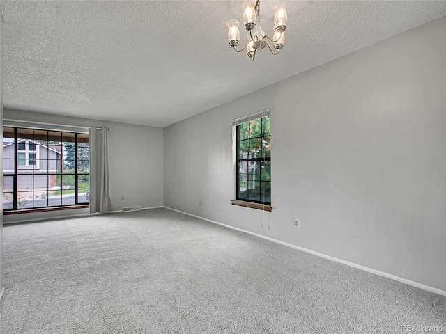 carpeted spare room with an inviting chandelier, baseboards, a textured ceiling, and visible vents
