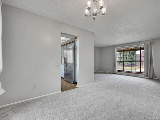 carpeted spare room featuring an inviting chandelier, baseboards, a textured ceiling, and visible vents