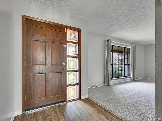 entrance foyer with a textured ceiling, baseboards, wood finished floors, and visible vents