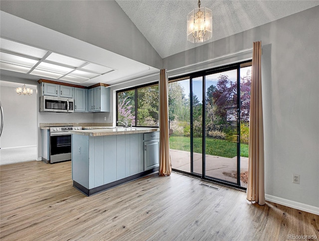 kitchen featuring stainless steel appliances, a peninsula, light wood-style flooring, and a notable chandelier