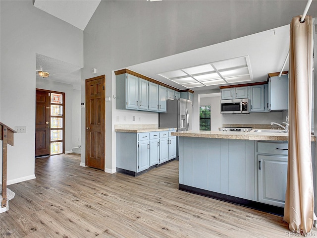 kitchen featuring a sink, light wood finished floors, stainless steel appliances, and a peninsula