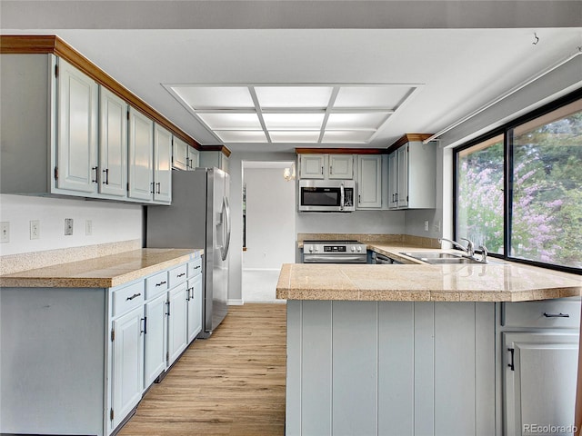 kitchen featuring appliances with stainless steel finishes, a sink, tile counters, light wood-style flooring, and a peninsula