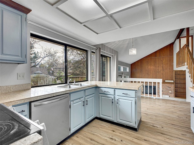 kitchen with a sink, dishwasher, tile counters, wood walls, and vaulted ceiling