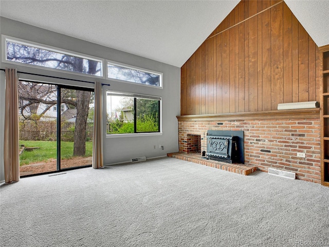 unfurnished living room with wooden walls, carpet floors, a textured ceiling, high vaulted ceiling, and visible vents
