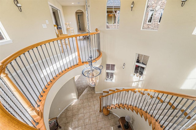 staircase featuring arched walkways, tile patterned floors, and a high ceiling