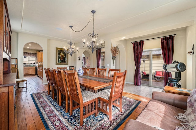 dining room with arched walkways, light wood-type flooring, and an inviting chandelier