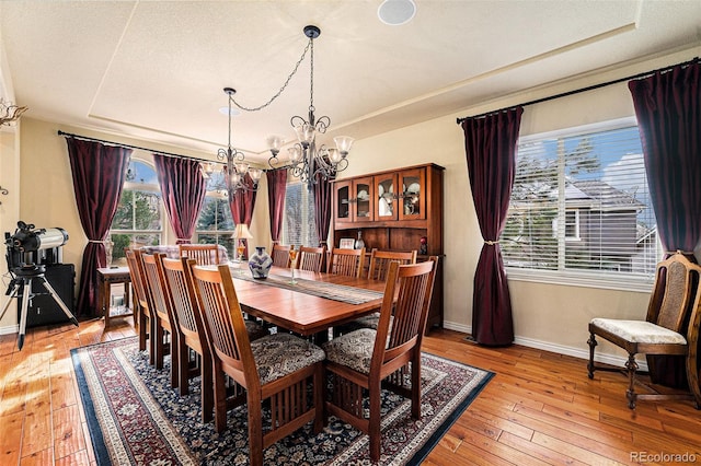 dining area featuring light wood-type flooring, a raised ceiling, baseboards, and a chandelier