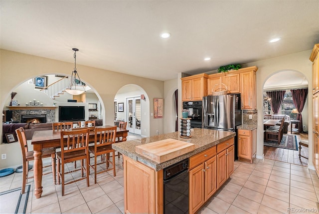 kitchen with a center island, recessed lighting, arched walkways, a stone fireplace, and light tile patterned floors