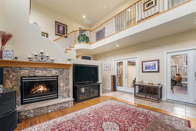 living area with visible vents, a stone fireplace, french doors, a high ceiling, and wood finished floors