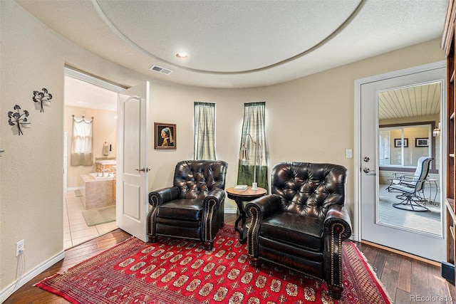 sitting room featuring baseboards, visible vents, wood-type flooring, and a textured ceiling