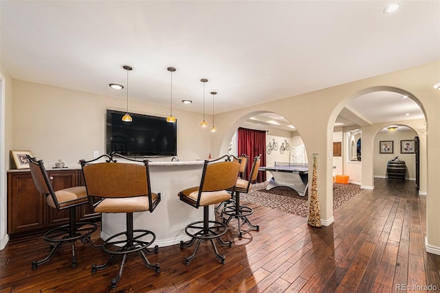 kitchen with decorative light fixtures, a kitchen breakfast bar, arched walkways, and dark wood finished floors