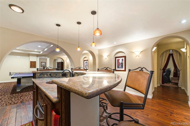 kitchen featuring a breakfast bar, arched walkways, dark wood-style flooring, and a spacious island