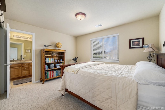 bedroom with visible vents, ensuite bathroom, and light carpet