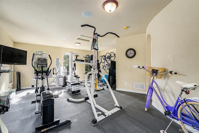 gym featuring visible vents, arched walkways, a textured ceiling, and baseboards