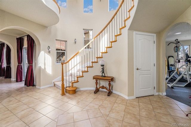 staircase featuring tile patterned floors, baseboards, arched walkways, and a towering ceiling