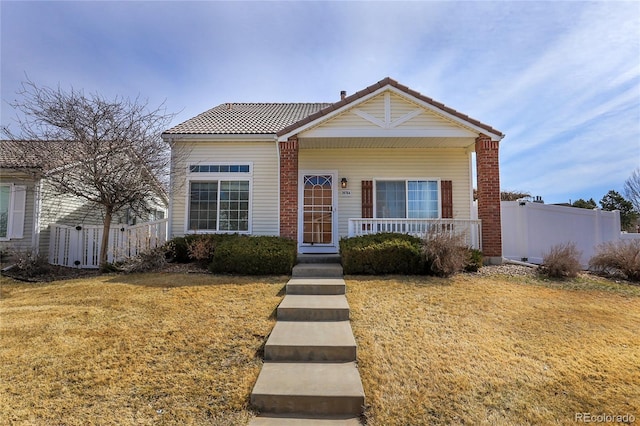 view of front of house with covered porch, a tiled roof, a front yard, and fence