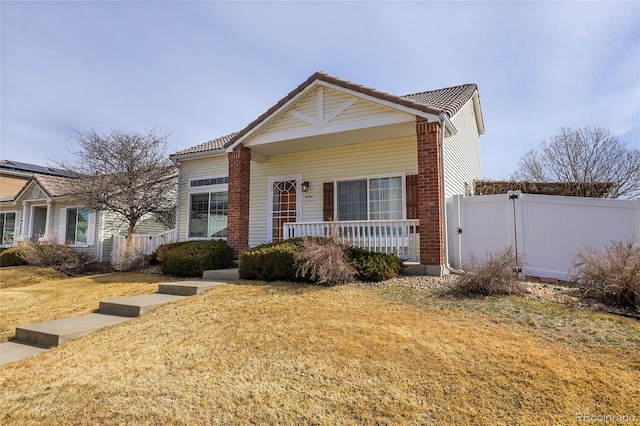 view of front facade with a tile roof, a front yard, fence, and covered porch