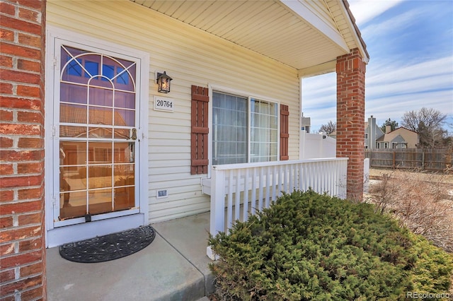 view of exterior entry featuring brick siding, covered porch, and fence