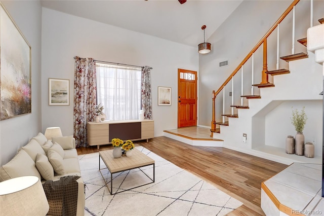 living area featuring stairway, light wood-style flooring, visible vents, and high vaulted ceiling