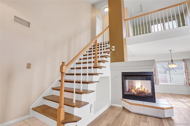 stairs with visible vents, wood finished floors, baseboards, a multi sided fireplace, and a towering ceiling