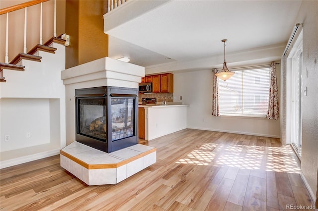 kitchen with light wood finished floors, decorative backsplash, a tiled fireplace, stainless steel microwave, and brown cabinets