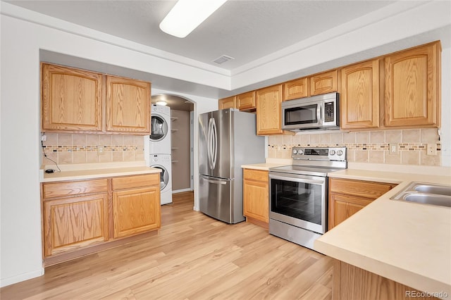 kitchen with light wood-type flooring, visible vents, stacked washer and dryer, stainless steel appliances, and decorative backsplash