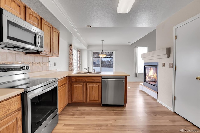 kitchen with light wood finished floors, appliances with stainless steel finishes, a peninsula, and a sink