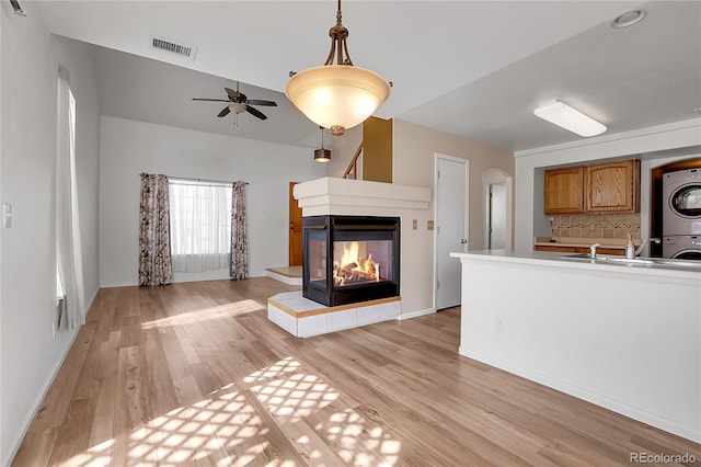 unfurnished living room with visible vents, a ceiling fan, light wood-style floors, stacked washer / dryer, and a multi sided fireplace