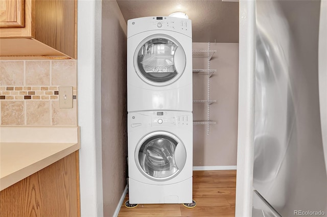 laundry room featuring laundry area, stacked washer / drying machine, baseboards, and wood finished floors