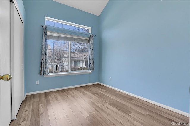 unfurnished bedroom featuring a closet, baseboards, wood finished floors, and vaulted ceiling