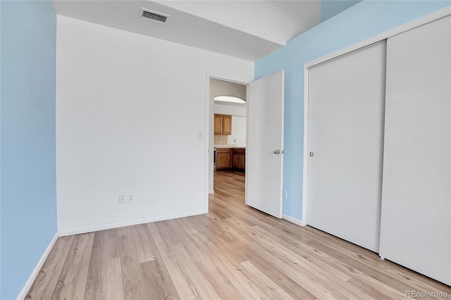 unfurnished bedroom with arched walkways, light wood-type flooring, a closet, and baseboards