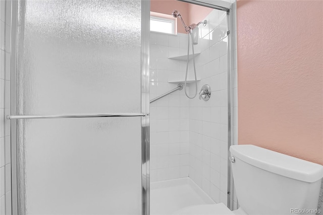 bathroom with a shower stall, toilet, and a textured wall