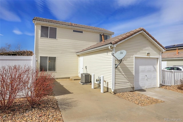 rear view of house with fence, a tile roof, concrete driveway, central AC unit, and an attached garage