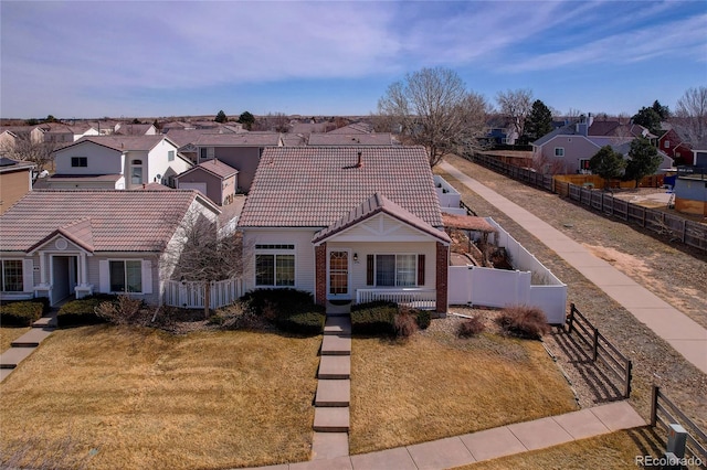 view of front facade featuring a residential view, fence private yard, a front lawn, and a tiled roof