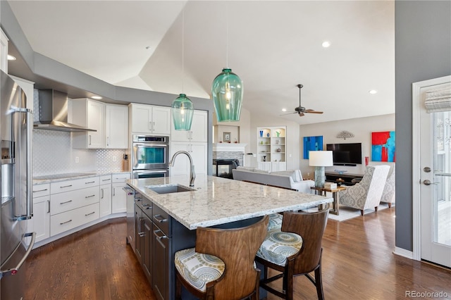 kitchen featuring a sink, white cabinets, vaulted ceiling, wall chimney range hood, and appliances with stainless steel finishes