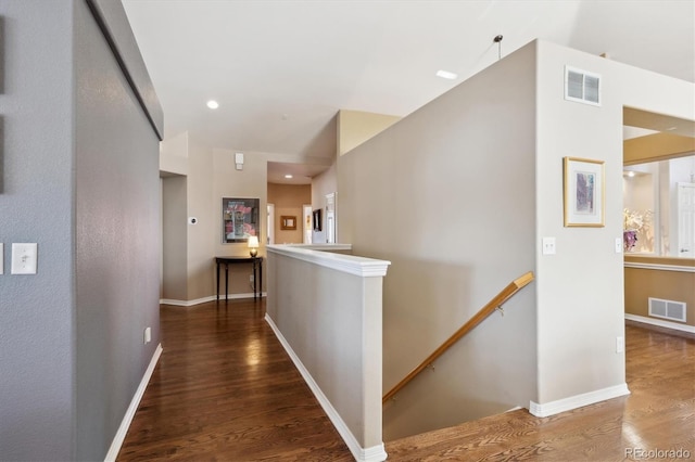 hall with baseboards, visible vents, an upstairs landing, and wood finished floors