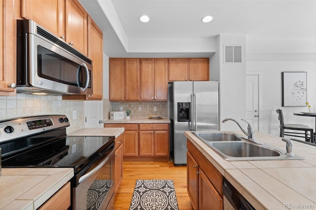 kitchen with backsplash, tile countertops, light hardwood / wood-style floors, sink, and stainless steel appliances