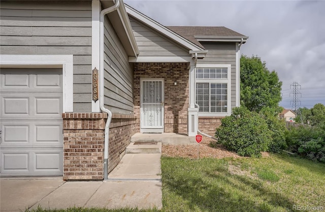 view of exterior entry featuring brick siding, a garage, and a yard