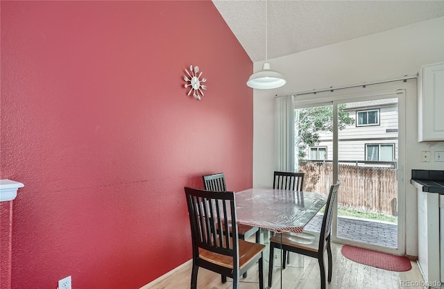 dining room with vaulted ceiling, light wood-style flooring, a textured ceiling, and baseboards