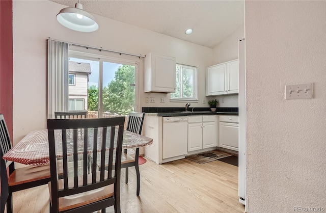 kitchen with white appliances, light wood-type flooring, dark countertops, white cabinets, and a sink