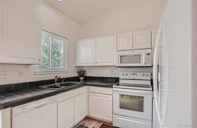 kitchen featuring white appliances, a sink, vaulted ceiling, white cabinetry, and tile countertops